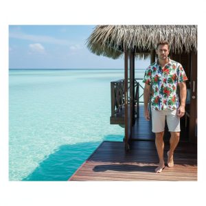 Man wearing vibrant parrot hawaiian shirt at tropical beach resort with palm trees and ocean background